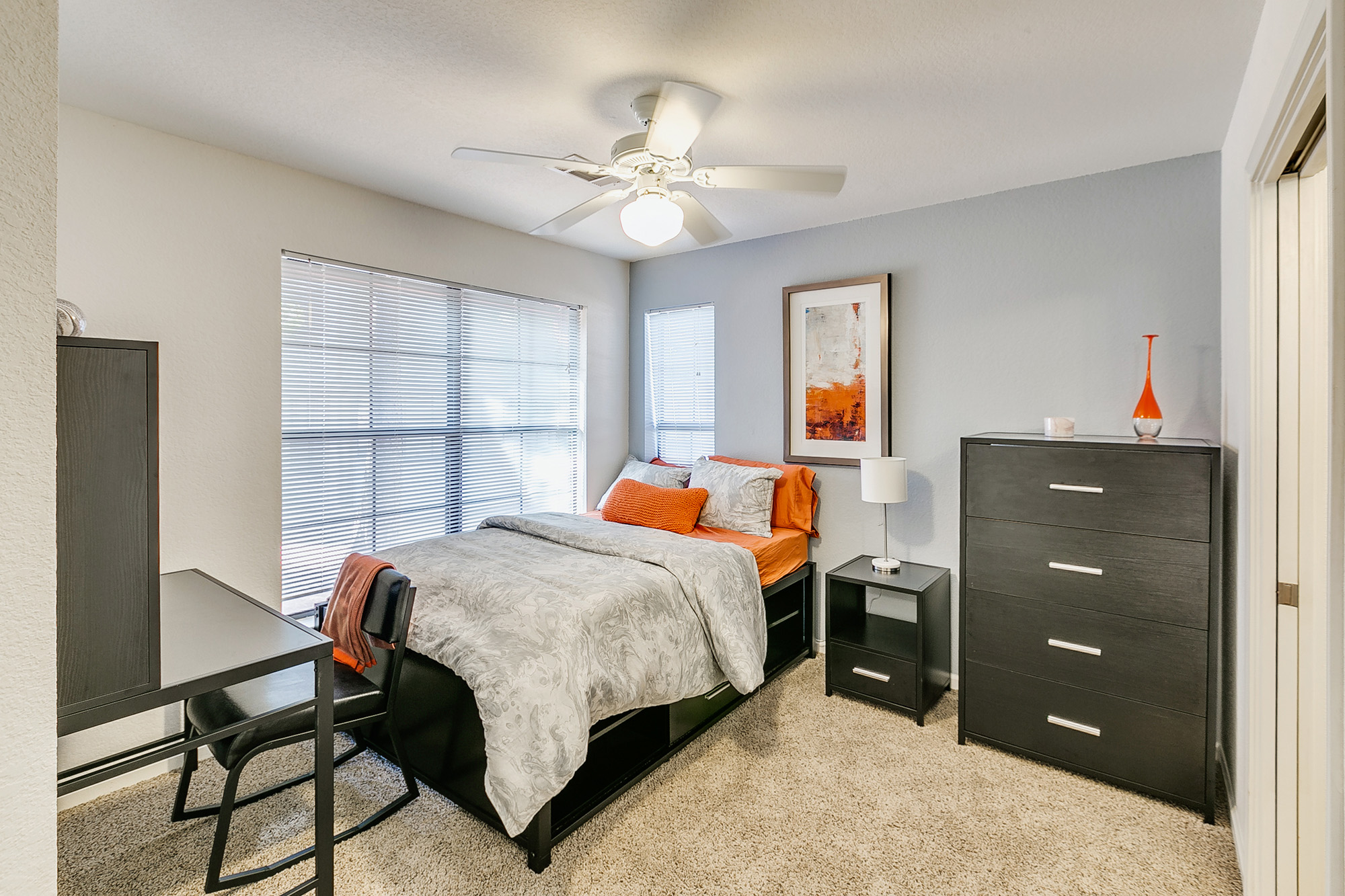 a bedroom with a bed and a desk and a fan