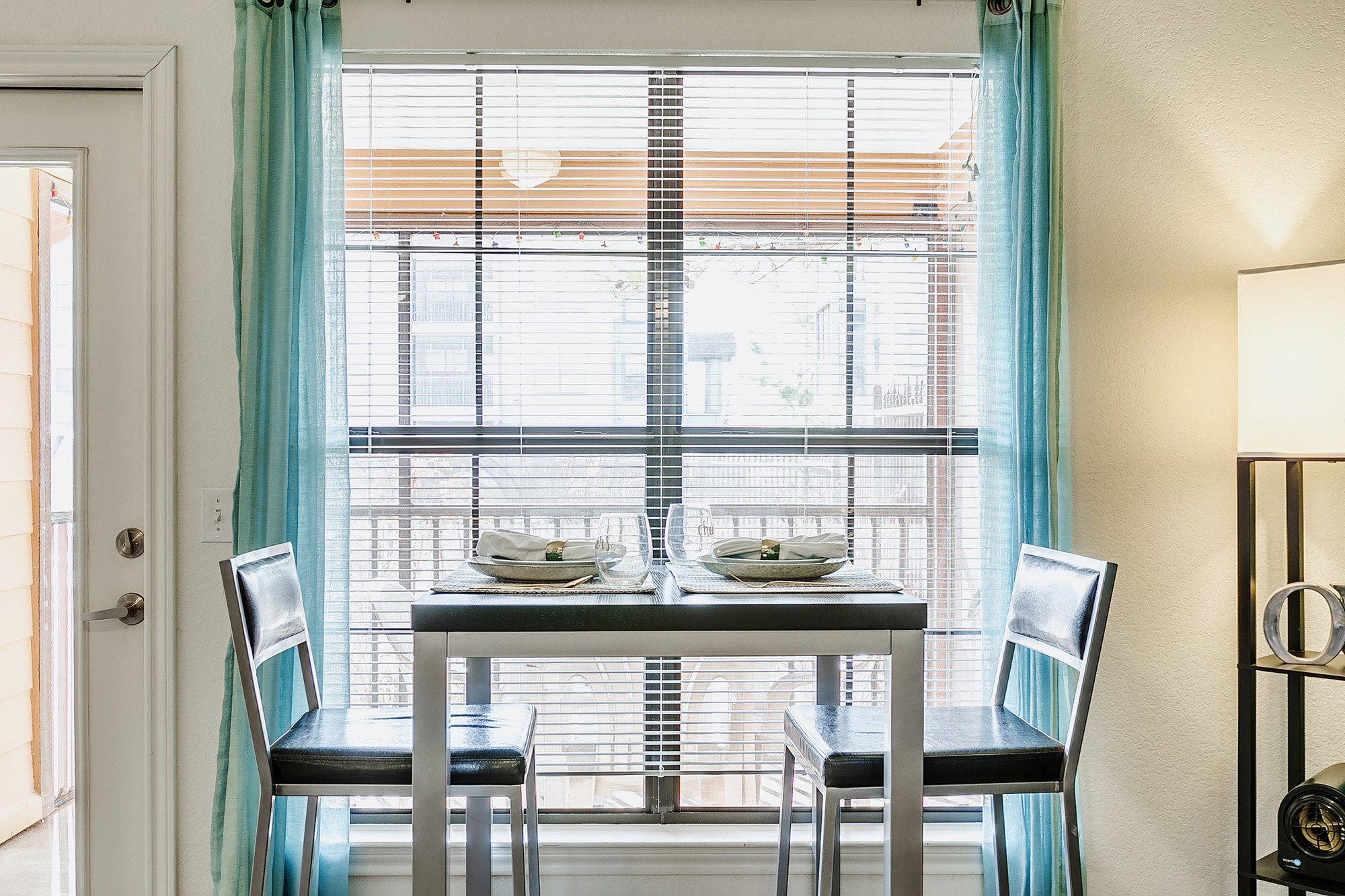 Table with two chairs near a window with teal curtains